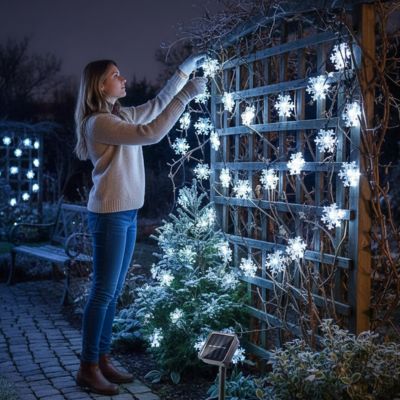 femme installe guirlande extérieur pour noël solaire flocons treillis