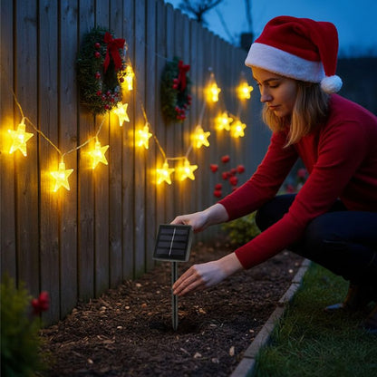 femme installe guirlande exterieur noel solaire étoiles sur clôture